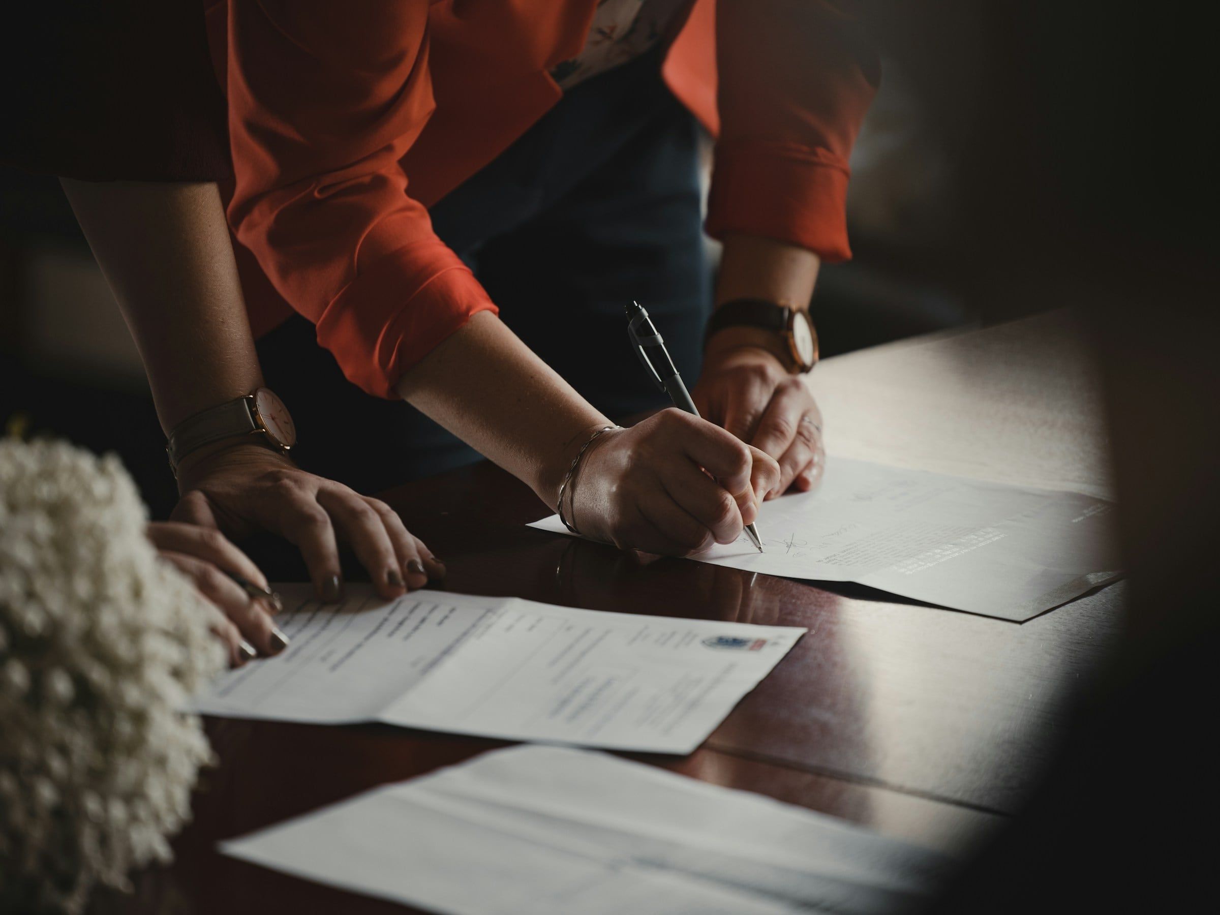Dos personas firmando documentos sobre una mesa durante la formalización de un acuerdo