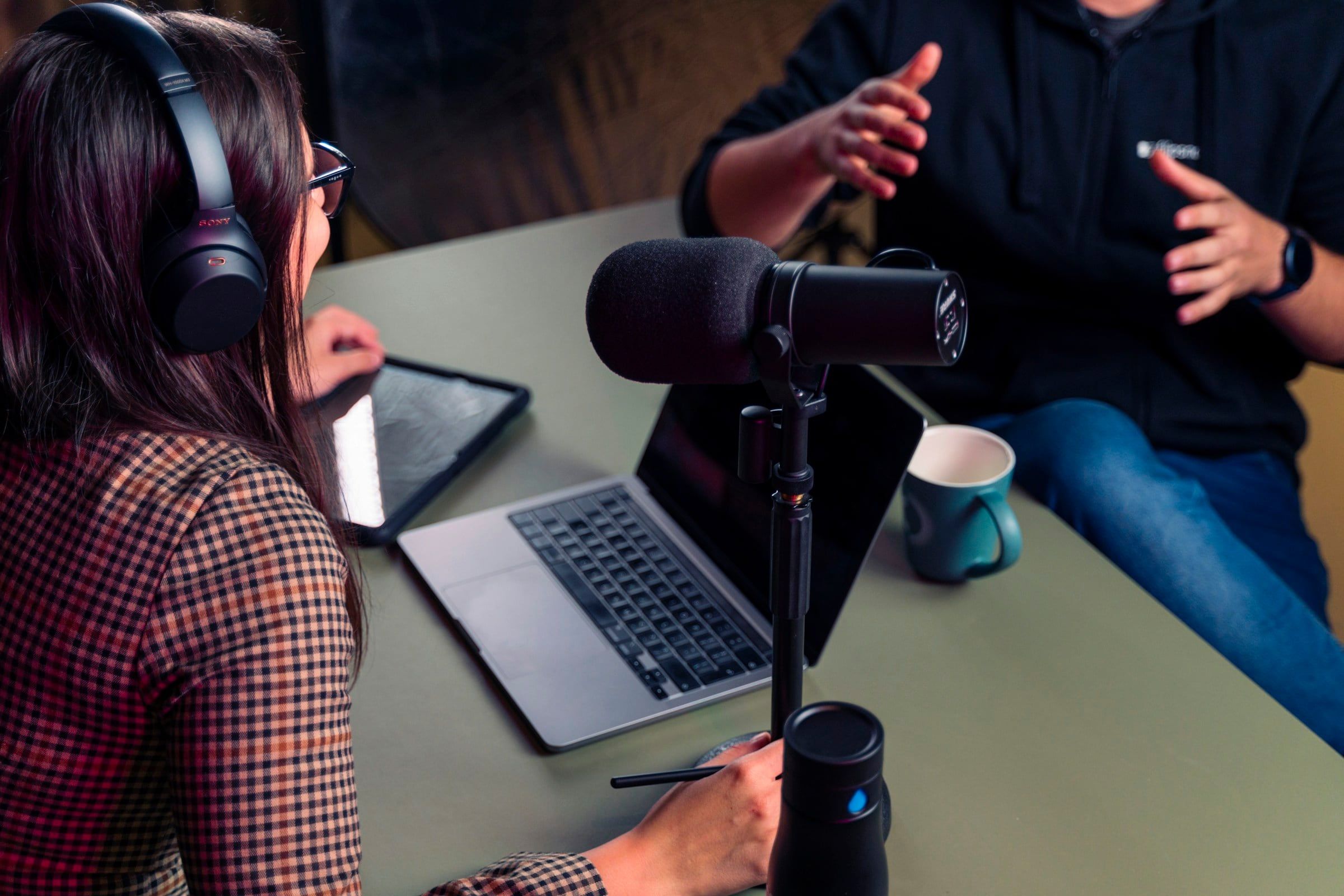 Dos personas grabando un episodio de pódcast frente a los micrófonos de la mesa